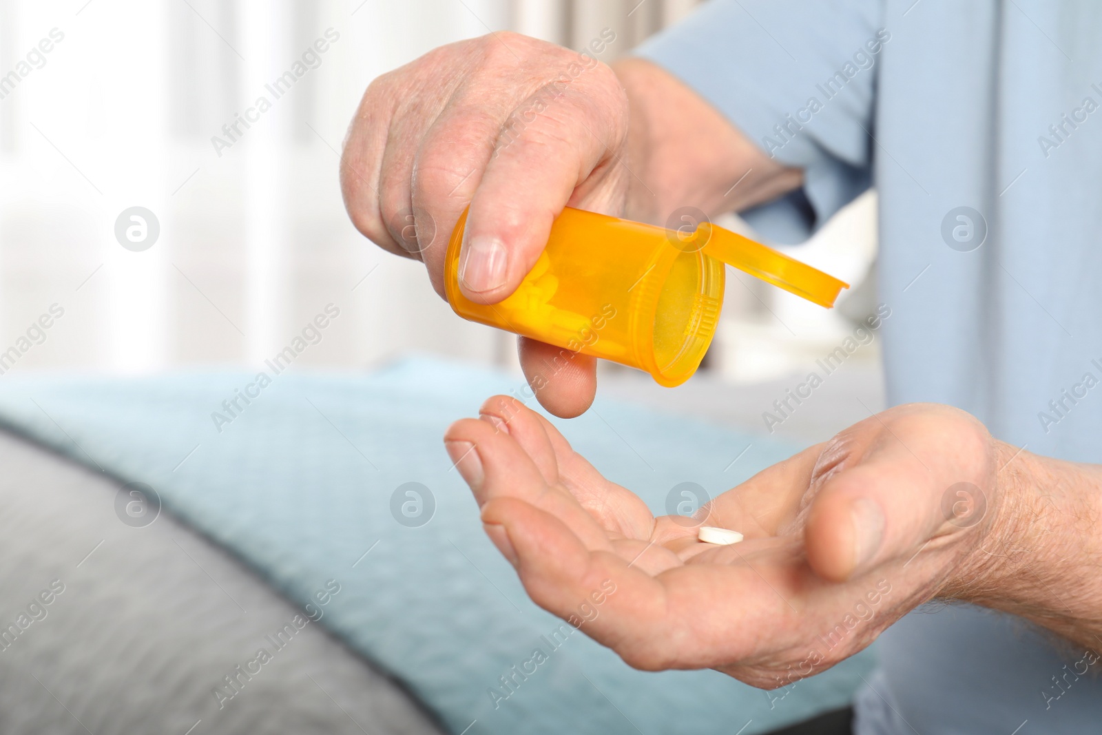 Photo of Senior man pouring pills from bottle into hand indoors, closeup