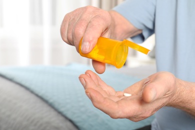 Photo of Senior man pouring pills from bottle into hand indoors, closeup