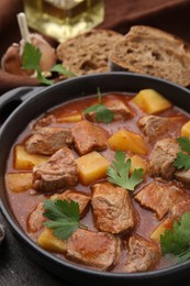 Delicious goulash in pot on wooden table, closeup