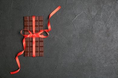 Tasty chocolate bar with red ribbon on dark background, top view