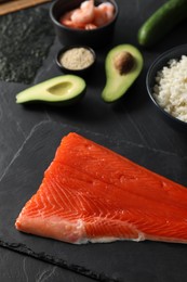 Fresh salmon for sushi and other ingredients on dark table, above view