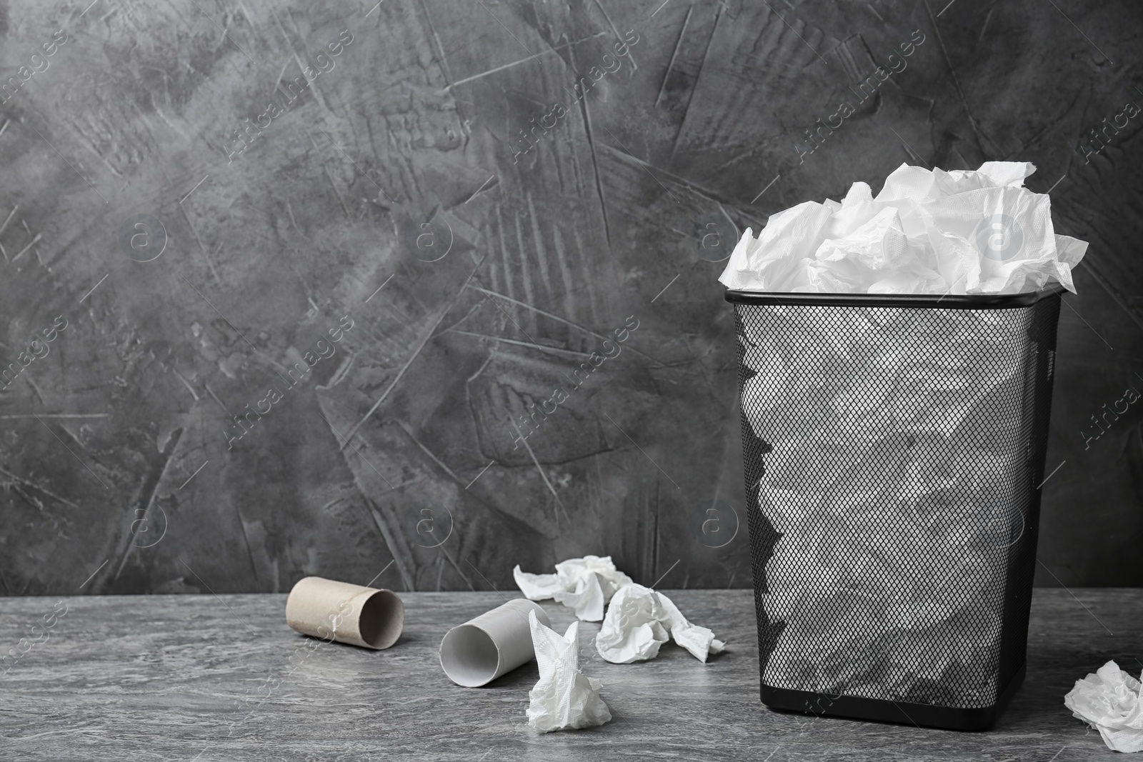 Photo of Trash bin with used toilet paper on floor near grey wall. Space for text