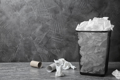 Photo of Trash bin with used toilet paper on floor near grey wall. Space for text