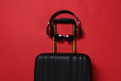 Photo of Stylish suitcase with sunglasses and headphones on color background, top view