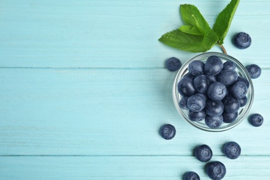 Glass bowl of tasty blueberries and leaves on color wooden table, flat lay. Space for text