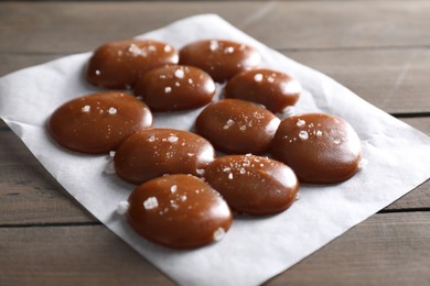 Photo of Tasty caramel candies and salt on wooden table, closeup