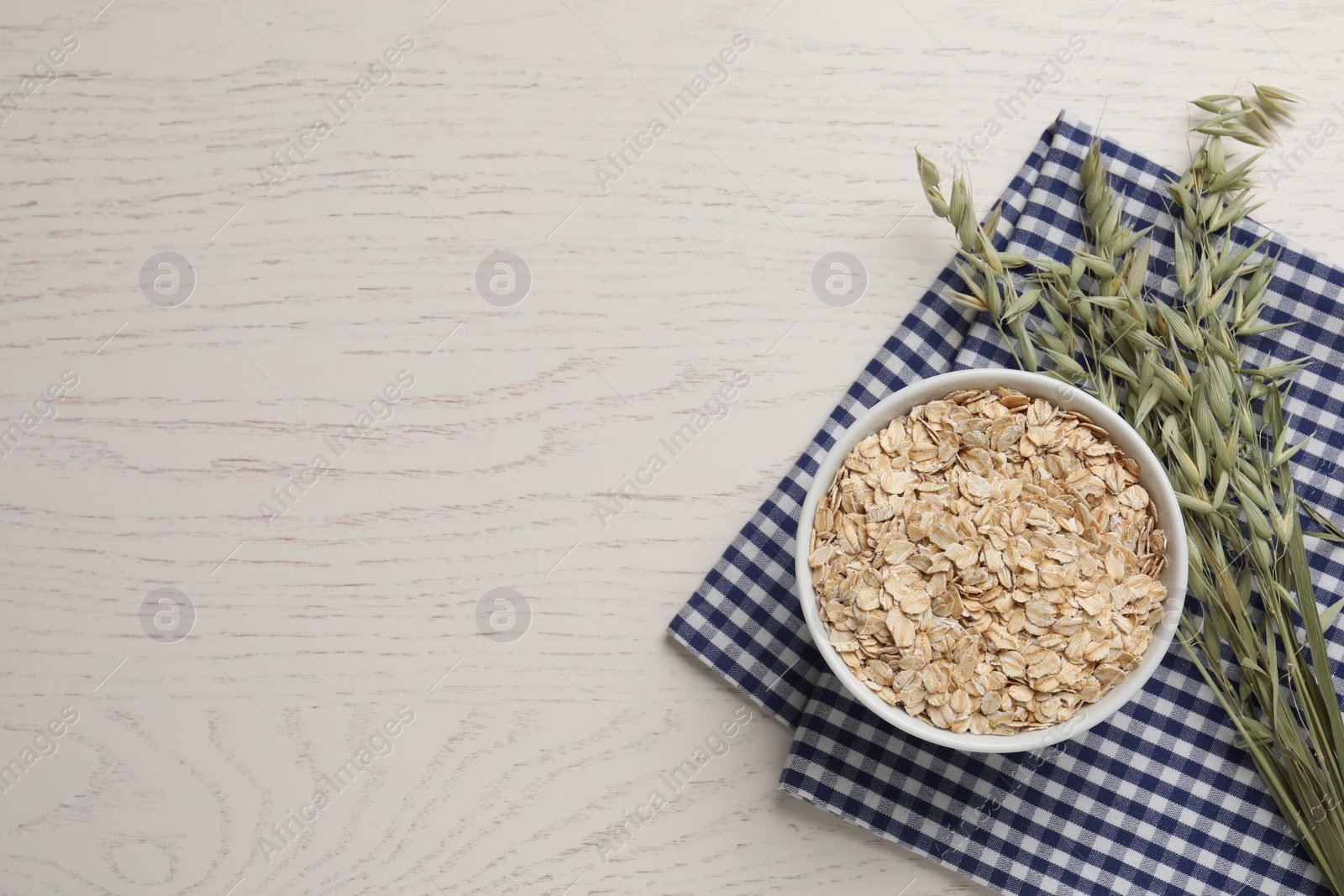 Photo of Bowl of oatmeal and branches with florets on white wooden table, top view. Space for text