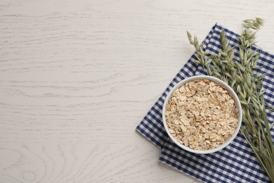 Bowl of oatmeal and branches with florets on white wooden table, top view. Space for text