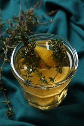 Photo of Glass of aromatic herbal tea with thyme and lemon on teal fabric