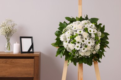 Photo of Wreath of flowers and frame with black ribbon on commode in room. Funeral attributes
