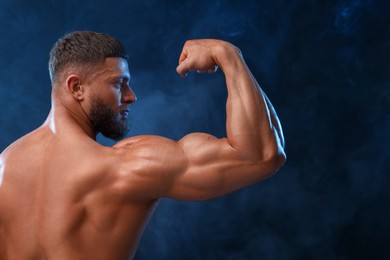 Young bodybuilder with muscular body in smoke on color background, back view