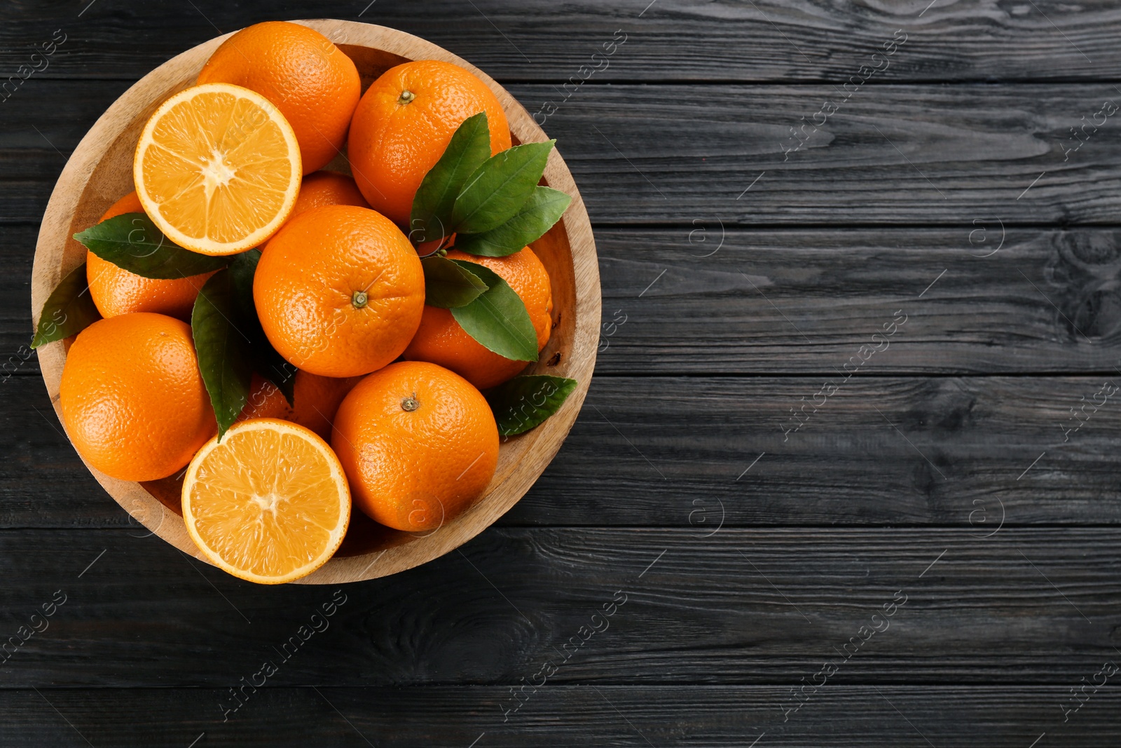 Photo of Delicious ripe oranges in bowl on black wooden table, top view. Space for text