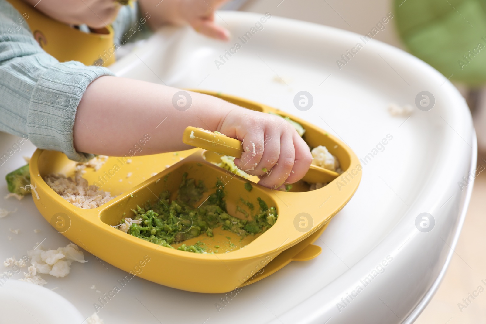 Photo of Little baby eating healthy food in high chair indoors, closeup