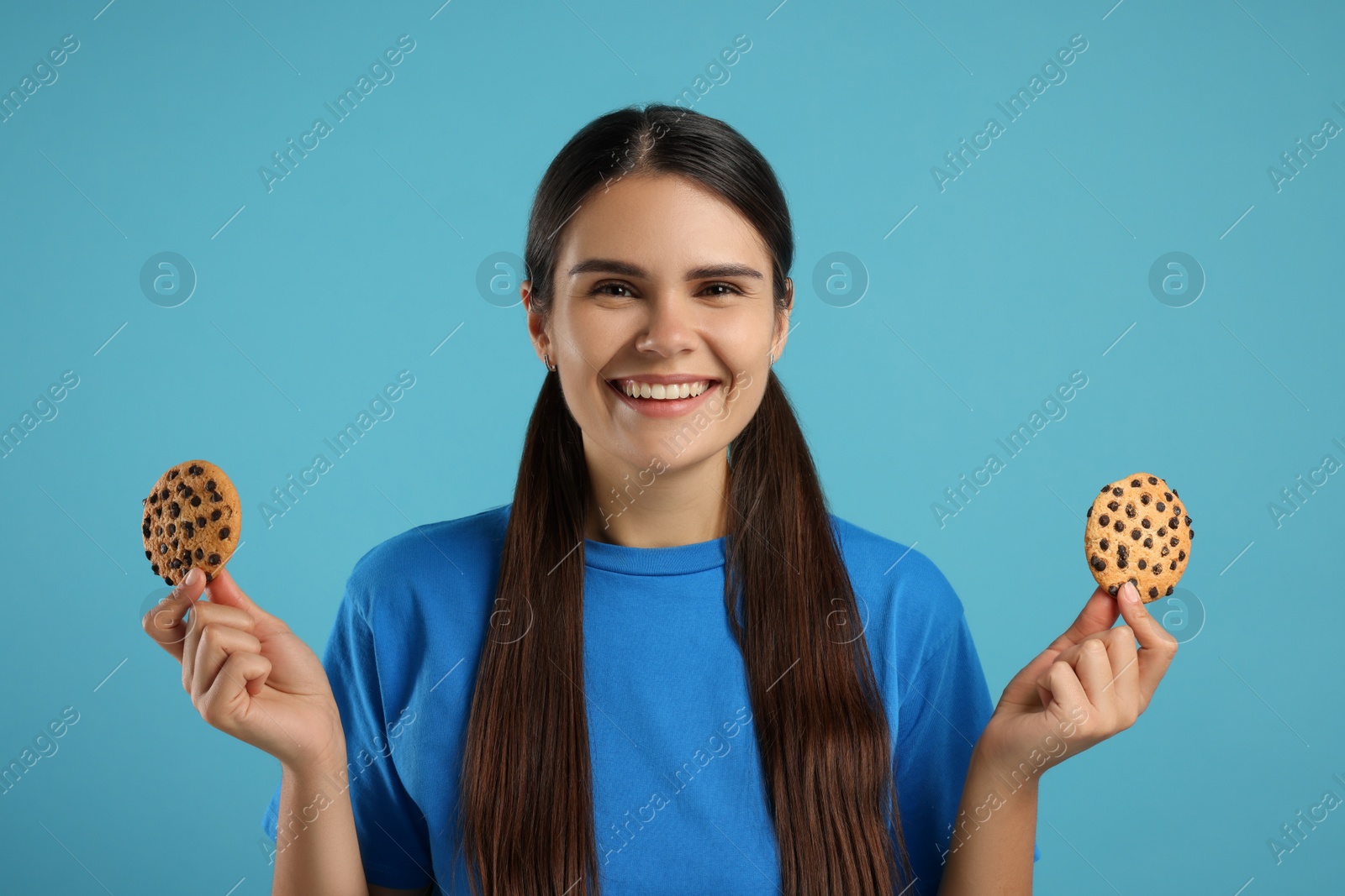 Photo of Young woman with chocolate chip cookies on light blue background