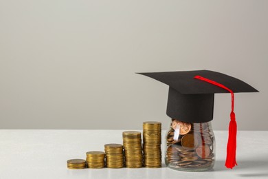 Photo of Scholarship concept. Graduation cap and stacked coins on white table