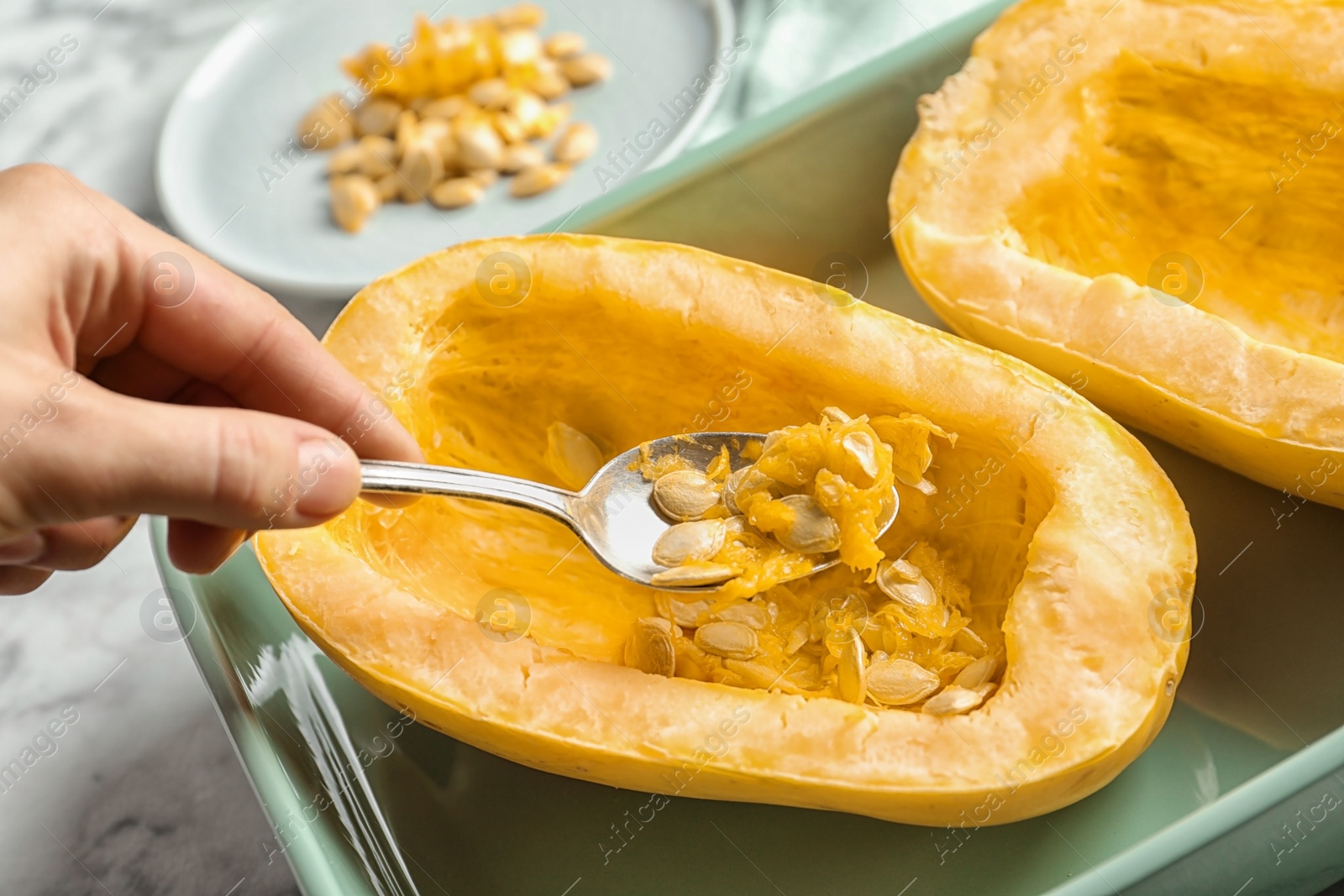 Photo of Woman removing seeds from spaghetti squash with spoon on table, closeup