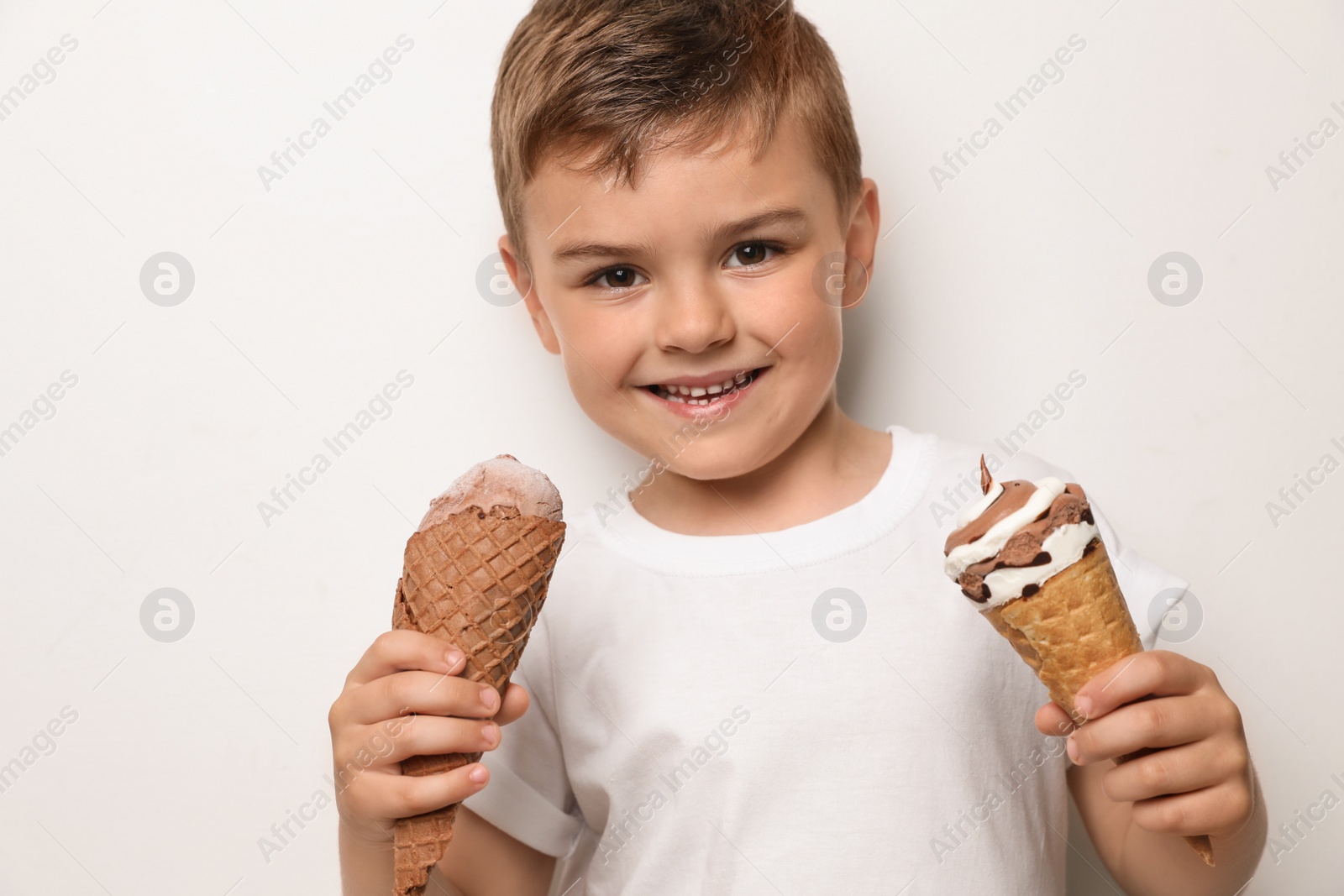 Photo of Adorable little boy with delicious ice creams against light background