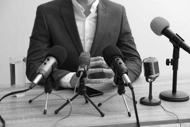 Image of Journalist conference. Businessman giving interview at table with microphones, closeup. Black and white effect