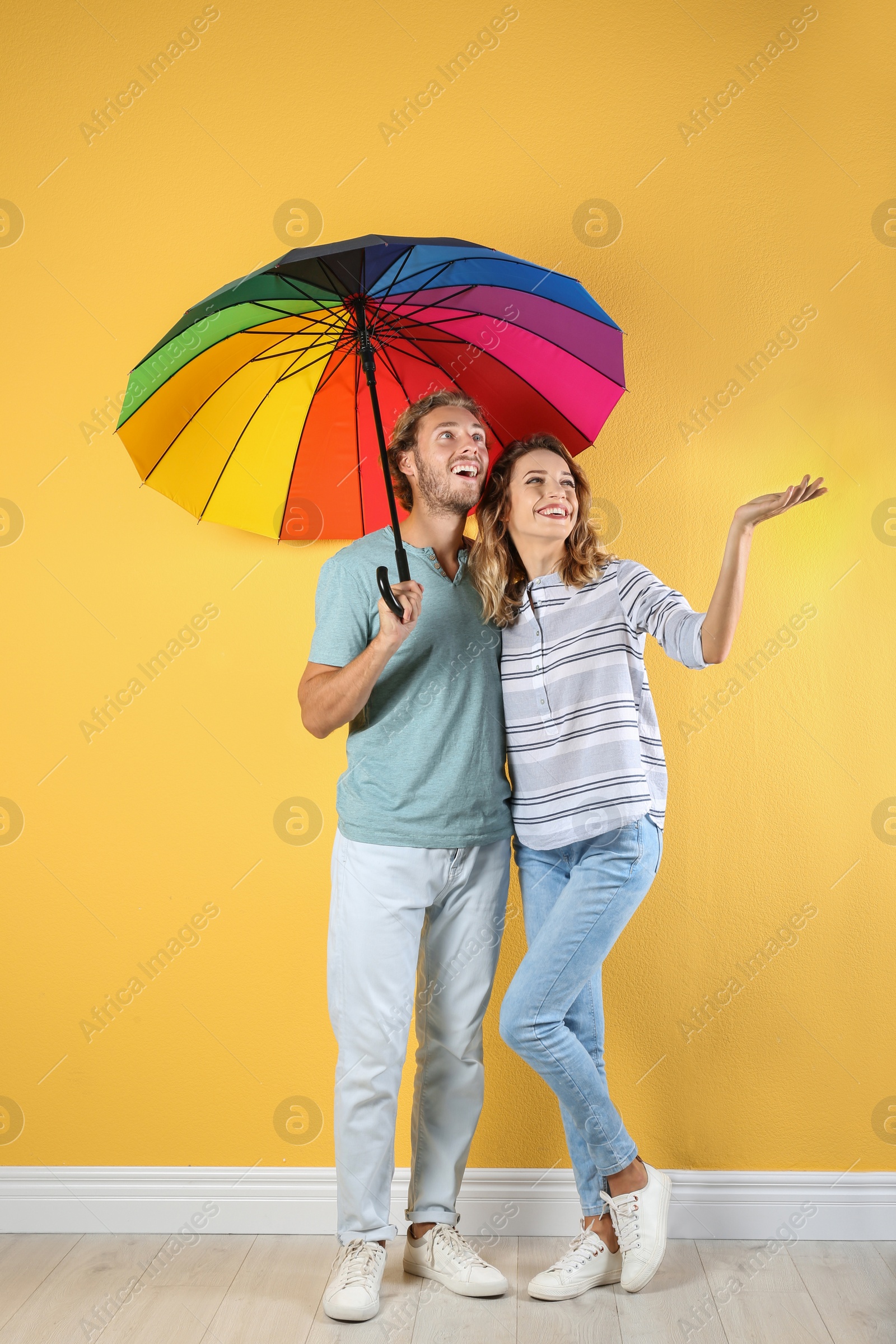 Photo of Couple with rainbow umbrella near color wall