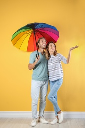 Couple with rainbow umbrella near color wall