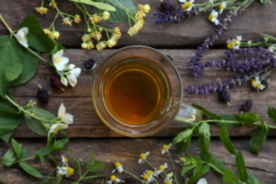 Photo of Cup of hot aromatic tea and different fresh herbs on wooden table, flat lay