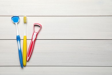 Photo of Different tongue cleaners and toothbrush on white wooden table, flat lay. Space for text