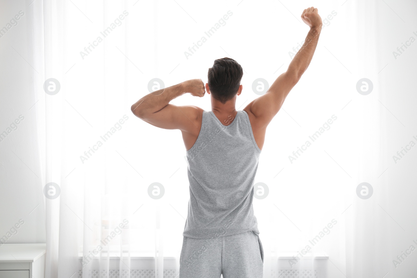 Photo of Man stretching near window at home. Lazy morning