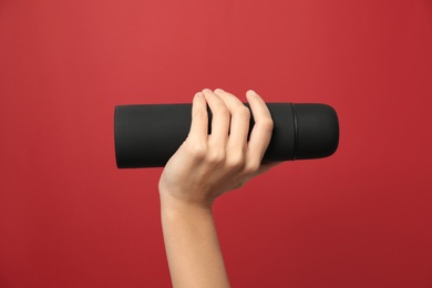 Photo of Woman holding modern black thermos on red background, closeup