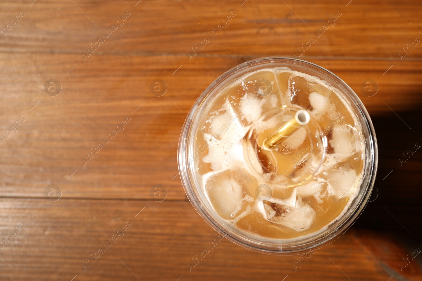 Photo of Refreshing iced coffee with milk in takeaway cup on wooden table, top view. Space for text