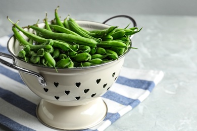 Photo of Fresh green beans in colander on grey marble table, closeup. Space for text