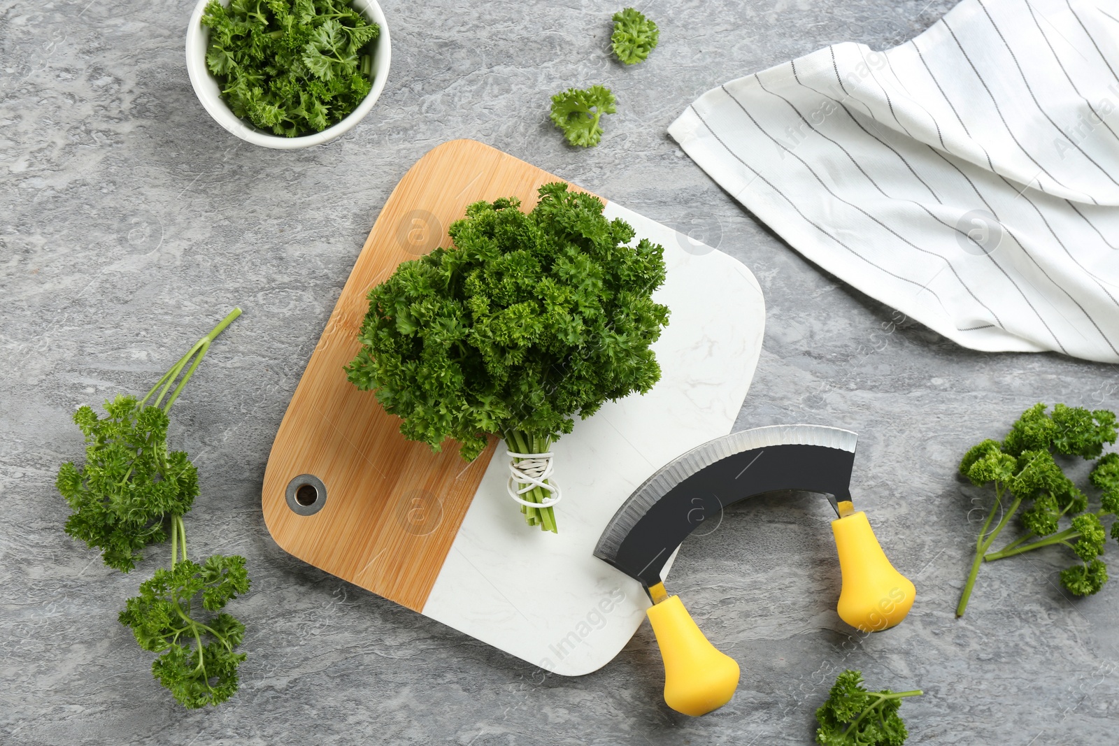 Photo of Fresh curly parsley, cutting board and mincing knife on grey table, flat lay