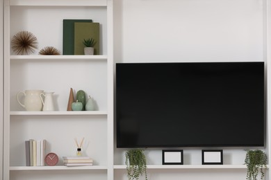 Photo of TV set and stylish shelves with decorative elements and houseplants near white wall. Interior design