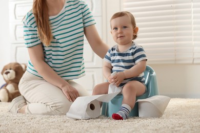 Mother training her child to sit on baby potty indoors