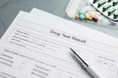 Photo of Drug test result form, pills and pen on grey table, closeup