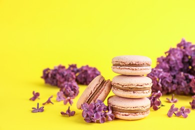 Delicious macarons and lilac flowers on yellow background, space for text