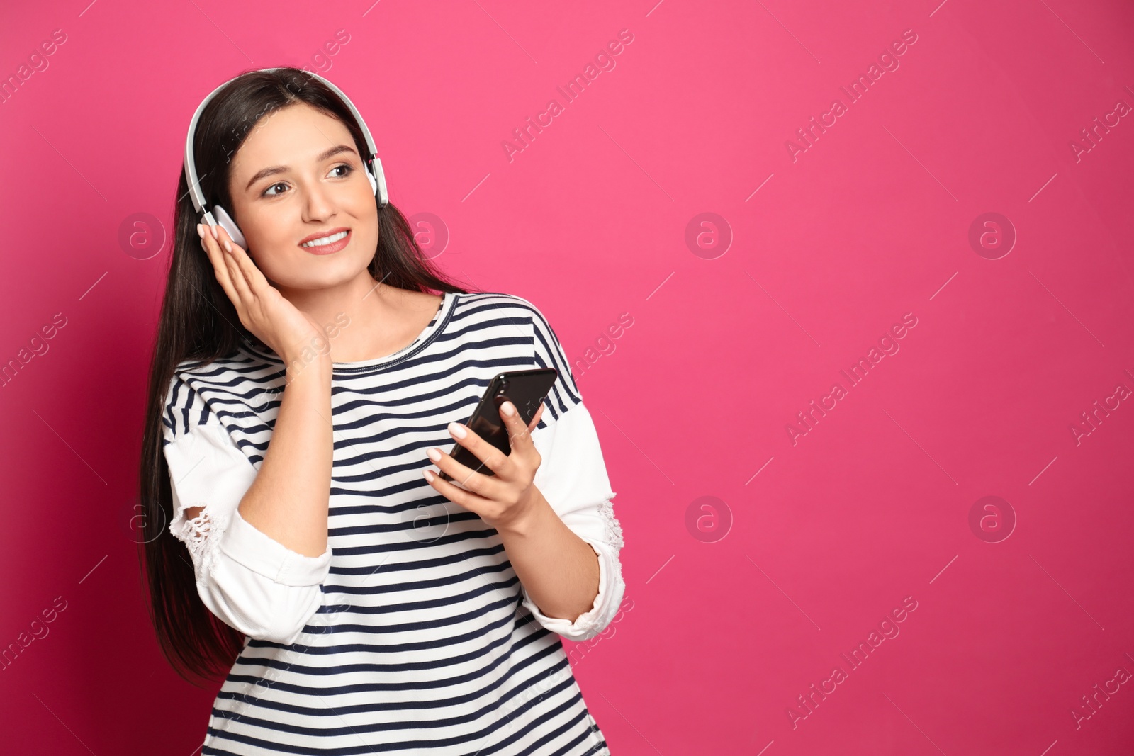 Photo of Young woman listening to audiobook on pink background. Space for text