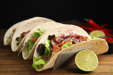 Photo of Delicious tacos with fried bacon and lime on wooden table, closeup