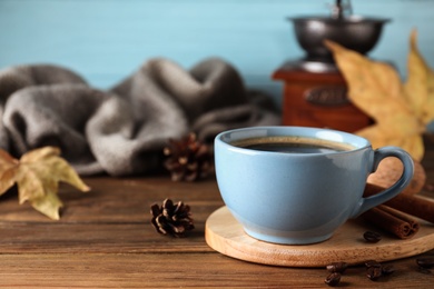 Cup of hot drink on wooden table against blue background, space for text. Cozy autumn atmosphere