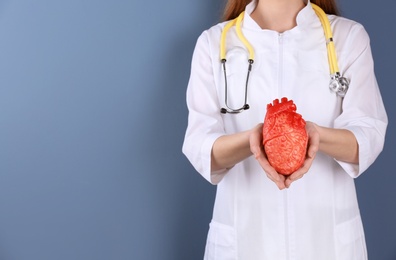 Photo of Doctor holding model of heart on color background. Prevent heart attack