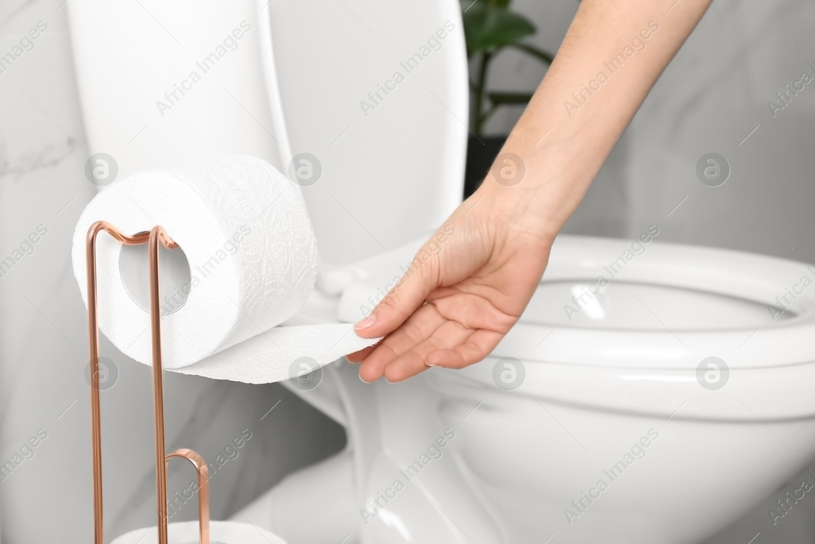 Photo of Woman taking toilet paper from roll holder in bathroom, closeup