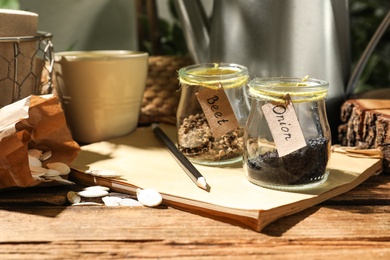Different vegetable seeds and notebook on wooden table