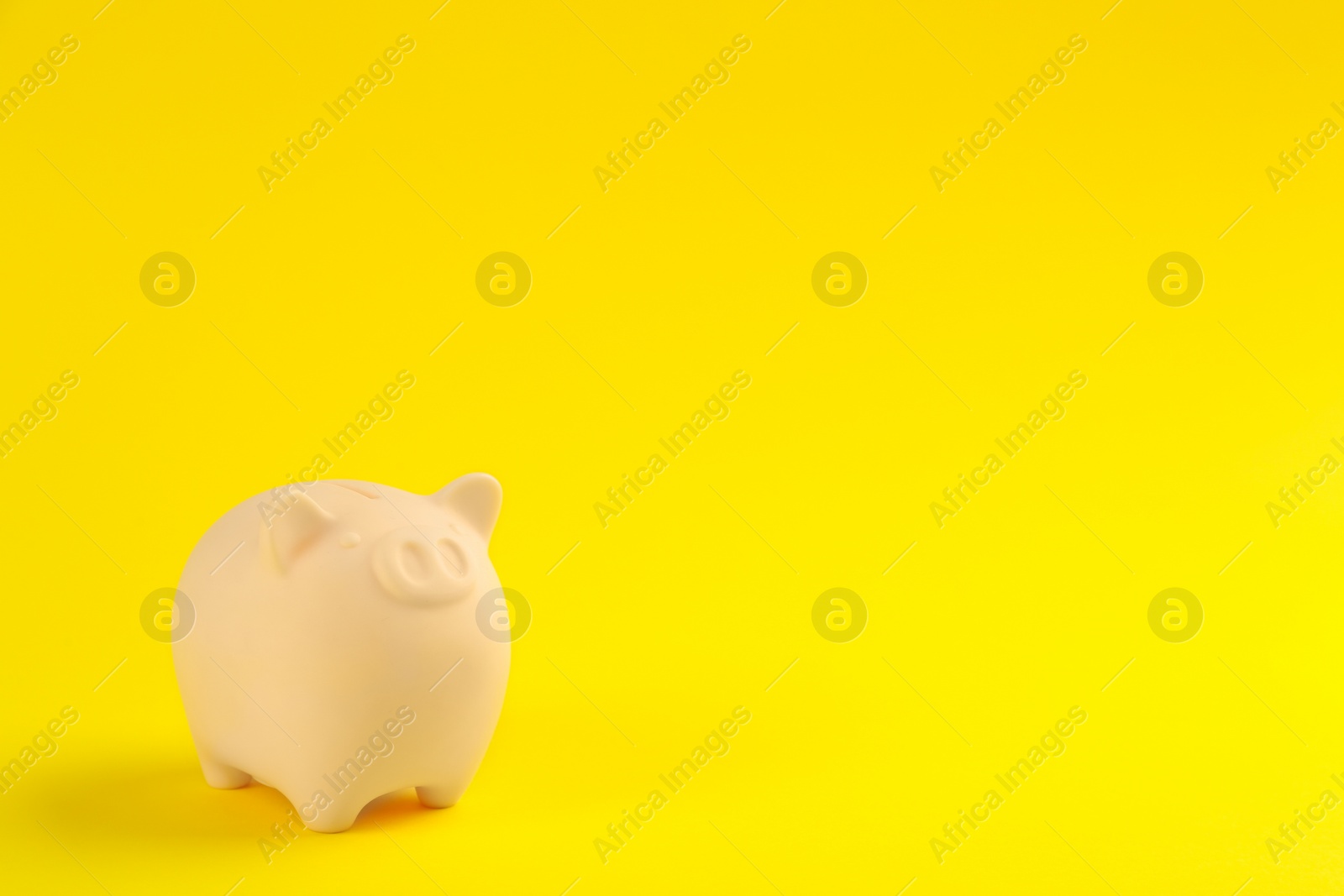 Photo of Beige piggy bank on yellow background. Space for text