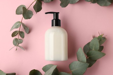 Photo of Bottle of liquid soap and eucalyptus branches on pink background, flat lay