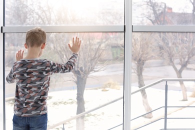 Photo of Lonely little boy near window indoors. Child autism