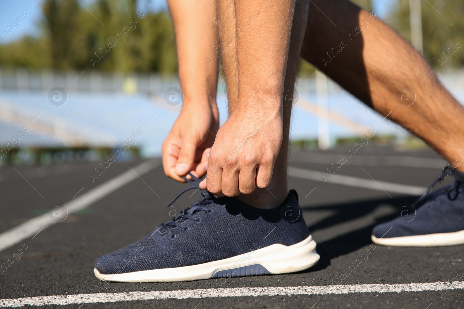 Photo of Sporty man tying shoelaces before running at stadium on sunny morning