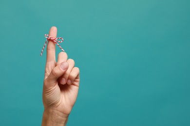 Woman showing index finger with tied bow as reminder on light blue background, closeup. Space for text