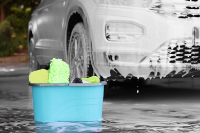 Photo of Car cleaning products and auto covered with foam outdoors, selective focus