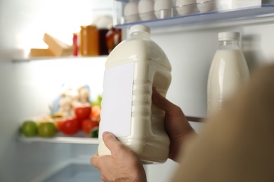Photo of Man holding gallon of milk near refrigerator, closeup