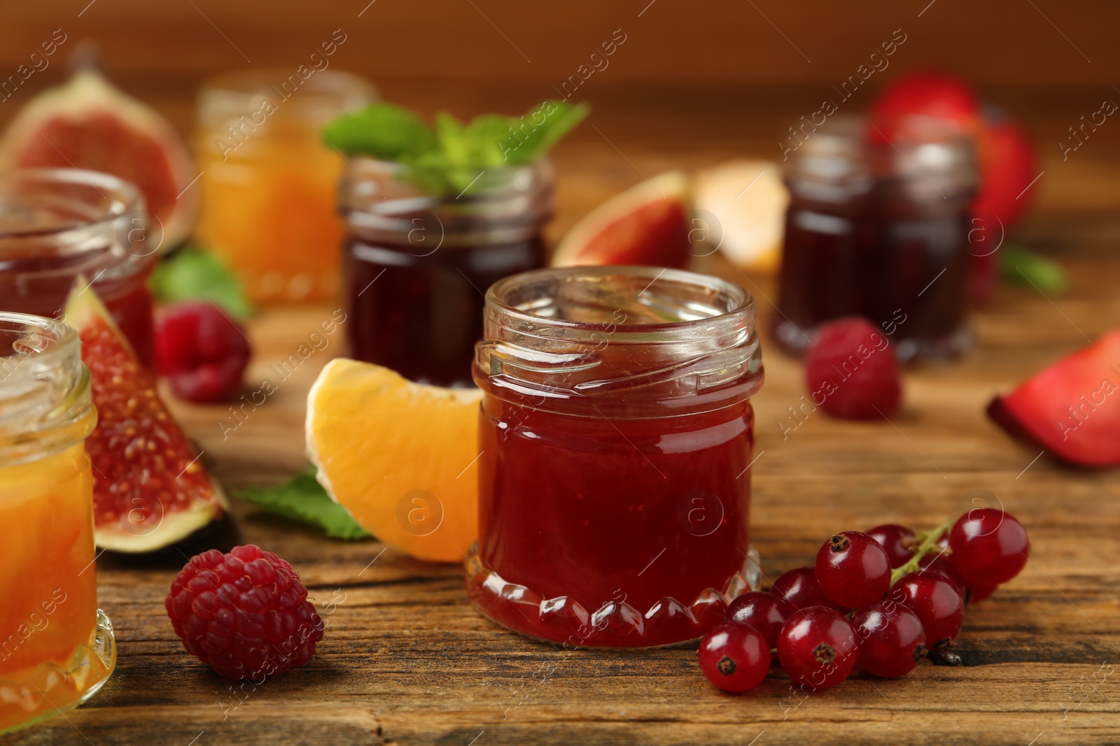 Photo of Jars of different jams and fresh ingredients on wooden table