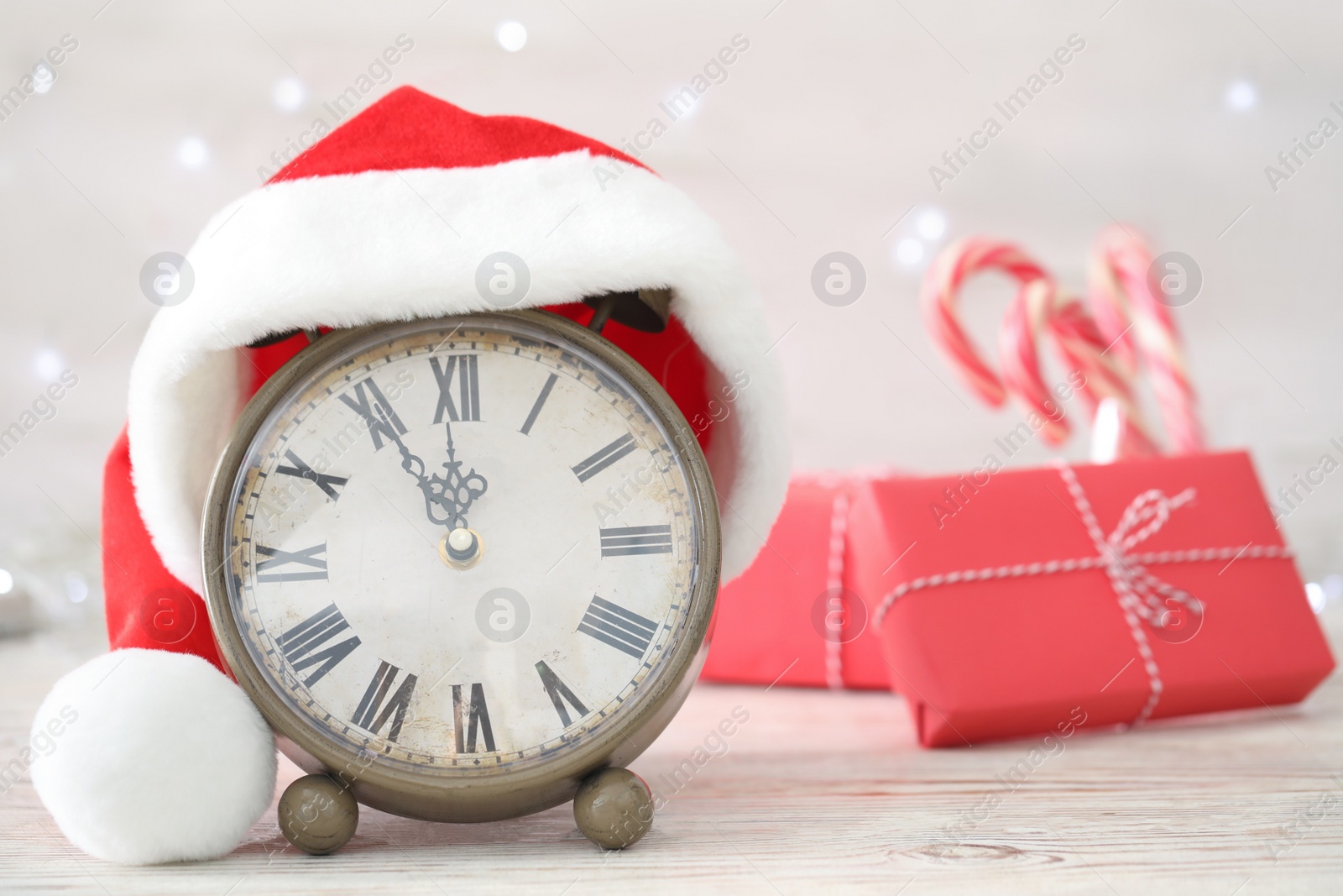 Photo of Vintage alarm clock with decor on white wooden table against blurred Christmas lights, closeup. New Year countdown